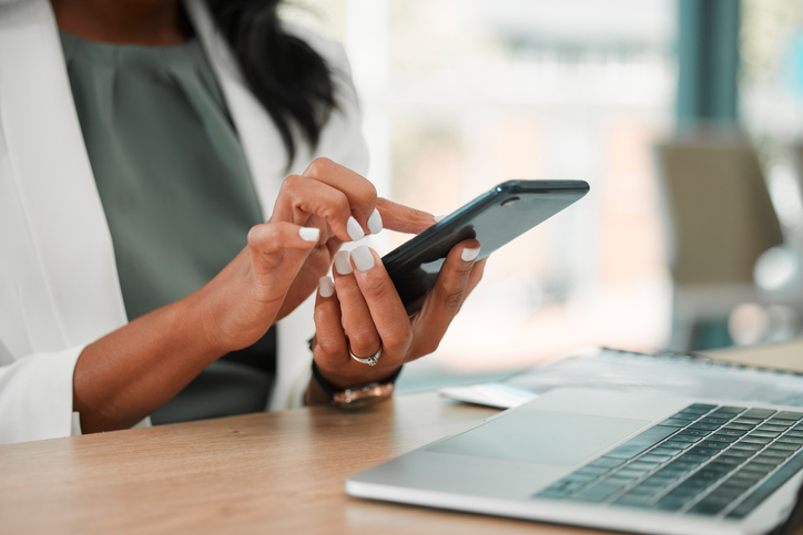 woman at desk making a call on her cell phone while sitting in front of her laptop